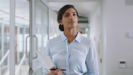 young-mixed-race-business-woman-walking-through-office-smiling-holding-documents-enjoying-successful-career-in-corporate-workplace-4k