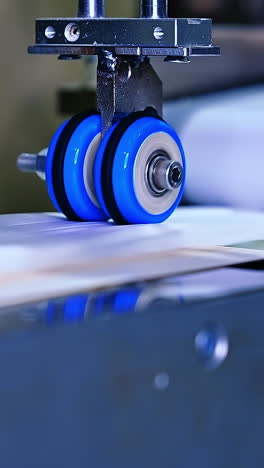 Little blue rollers spin to make recesses on the diaper surface. Quickly rotating shafts of the conveyor line at the diaper manufacturing close up. Vertical video