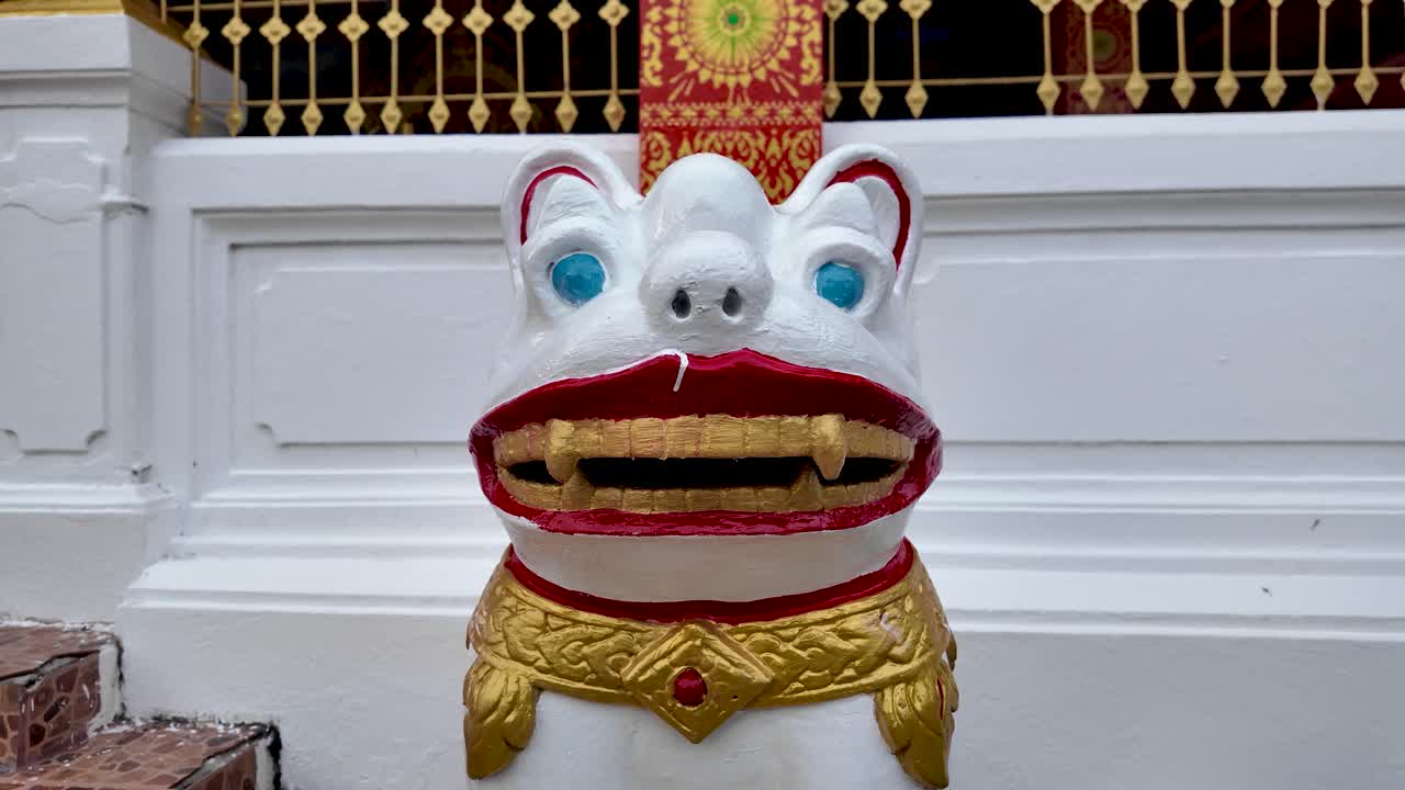 Una statua bianca di un leone guardiano con dettagli dorati si erge all'ingresso del tempio Wat Phonxay Xayxana SongKham a Luang Prabang, Laos