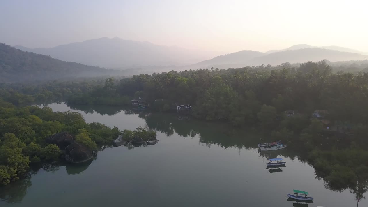 denso bosque reflejado a través de agua prístina con cadenas montañosas en el fondo durante un día brumoso en la playa de palolem, canacona, goa del sur, india