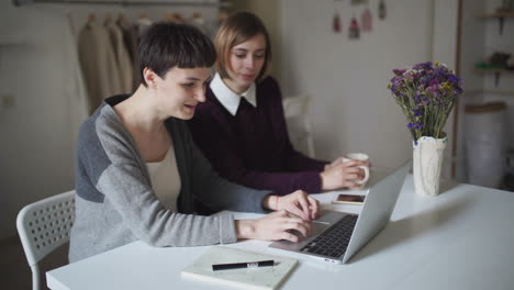 Two-woman-students-sitting-at-table-and-using-notebook-for-online-learning