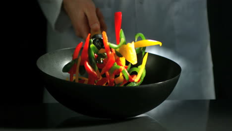 chef tossing wok of sliced peppers