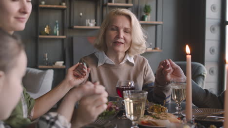 ältere frau, die am esstisch sitzt und vor dem essen mit ihrer familie zu hause betet