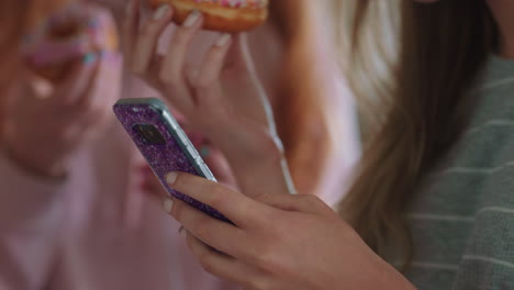 Nahaufnahme-Eines-Teenager-Mädchens,-Das-Sein-Smartphone-Nutzt,-Um-In-Sozialen-Medien-Zu-Surfen-Und-Freunden-Eine-SMS-Zu-Schicken,-Die-Rumhängen-Und-Donuts-Essen