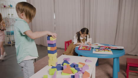 little boy in a montessori school playing with foam building blocks while little girl sitting at desk and drawing 1