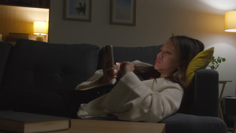 Woman Spending Evening At Home Lying On Sofa With Mobile Phone Scrolling Through Internet Or Social Media 3