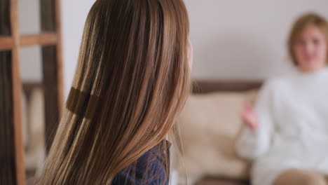 side view of specialist with long hair taking notes while engaged in thoughtful conversation with patient seated in background, hand raised in expressive gesture during calm therapy session