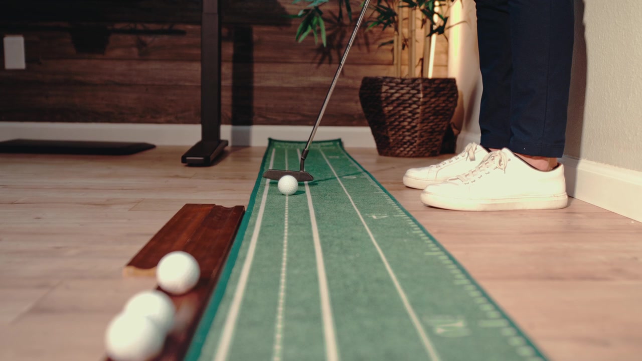 Golfista che colpisce il putt verso la telecamera nell'ufficio di casa su un tappetino da putting per la pratica. Video di allenamento di golf, contenuti di esercizi di putting e promozioni per la pratica a casa, ripresa statica in slow motion 4k.