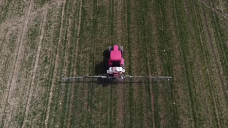 aerial view of red farming tractor spraying on the cultivated field with sprayer, herbicides and pesticides insecticide to the green field plowed land