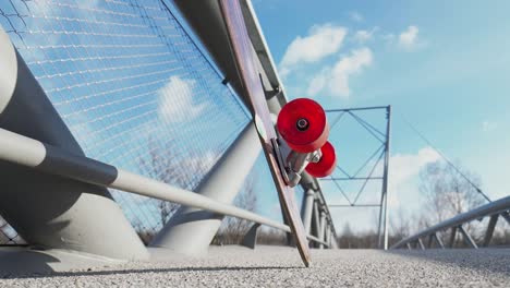 Slow-motion-shot-of-a-longboard-leaning-against-the-railing-of-a-pedestrian-bridge-and-feet-approaching-the-railing