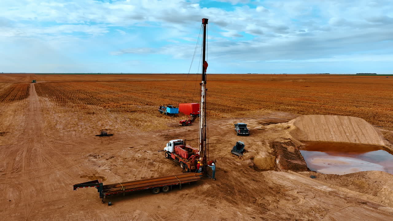 Site in the field with orange ground used at oil production. Two men work at the truck with derrick for drilling.
