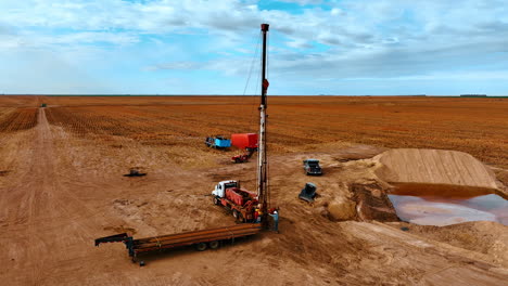 site in the field with orange ground used at oil production. two men work at the truck with derrick for drilling.