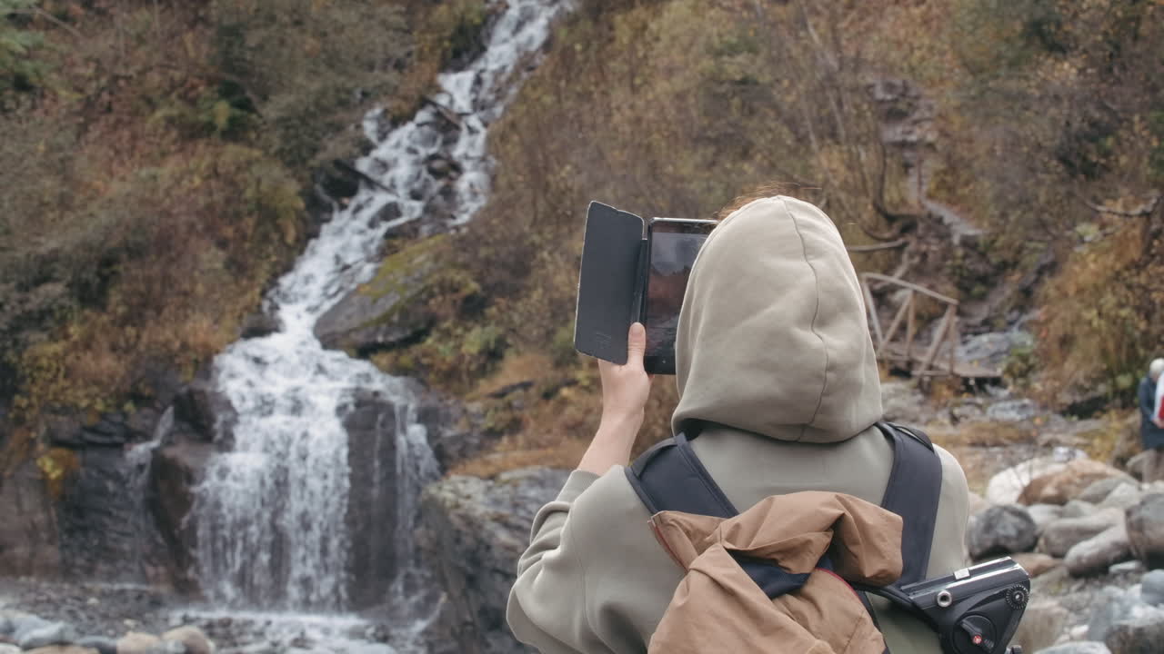 mujer tomando una foto de una cascada en la montaña