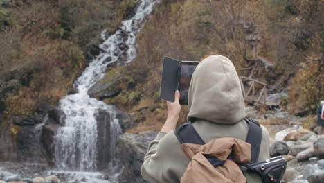 woman taking photo of waterfall in mountain