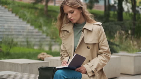 estudiante caucásica escribiendo en un cuaderno en el parque.