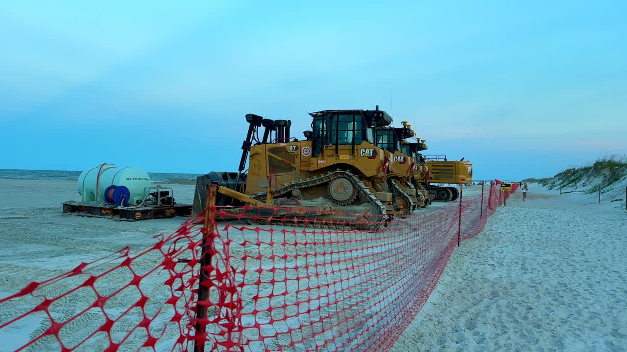 Bulldozers parked in sand near construction fencing, beach reclaim