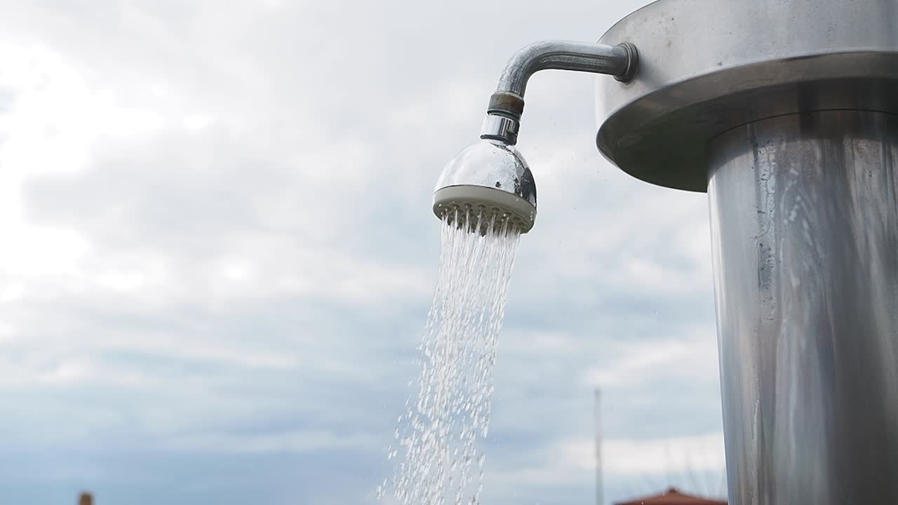 Soffione doccia esterno con getto d'acqua su cielo nuvoloso