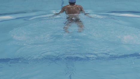 back view of young swimmer swimming in the pool, dive and doing frog style swim