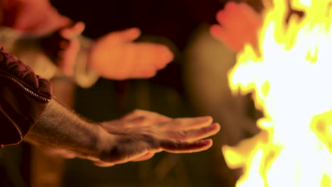 primer plano de un hombre calentando sus manos en el fuego del campamento