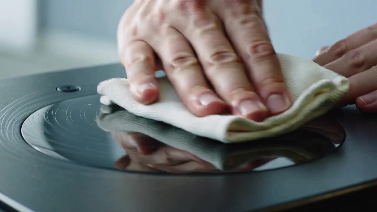 Approaching hand holding folded white rag wiping across black top, pressing, polishing shiny circle