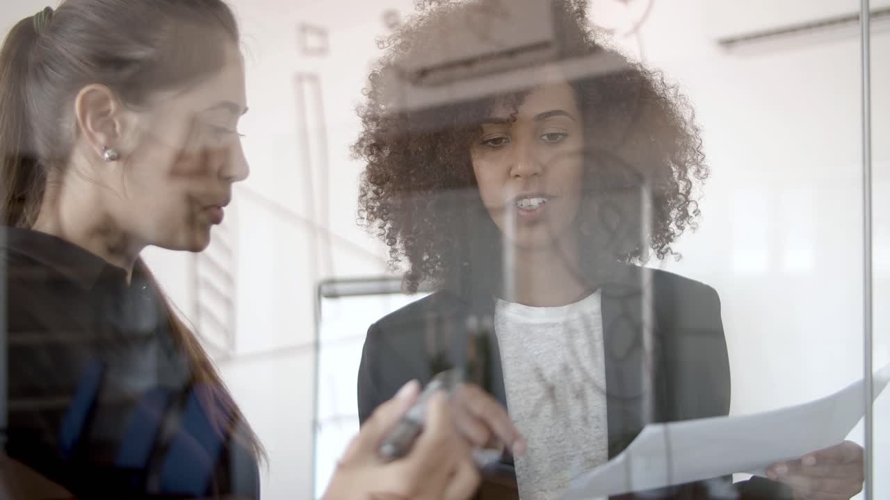 Two young managers drawing infographics on glass board