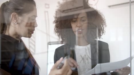 Two-young-managers-drawing-infographics-on-glass-board