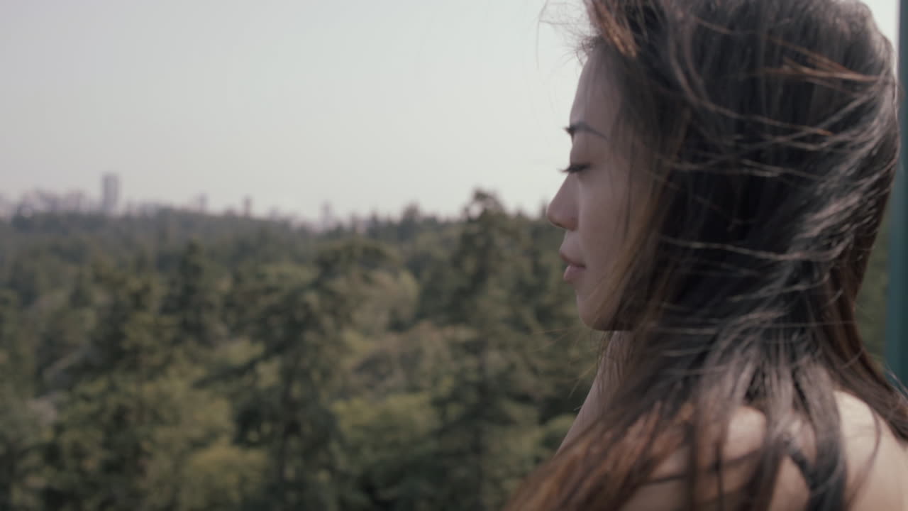 cerca de una atractiva chica asiática con largo cabello negro de pie en el puente lions gate, en el centro de vancouver en el fondo, cámara lenta