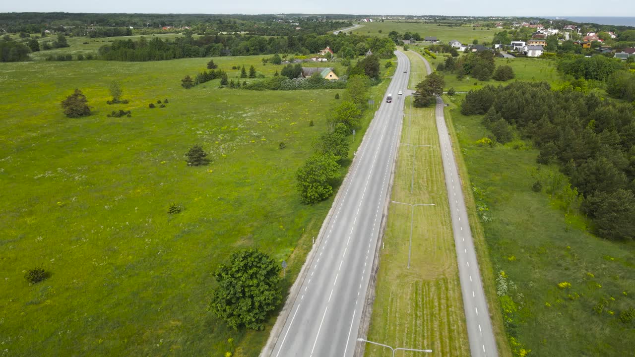 Gorgeous aerial drone flying over and gliding above a rural countryside highway or road that has a bicycle lane or pedestrian road separated from it with a grassy field during a cloudy day.