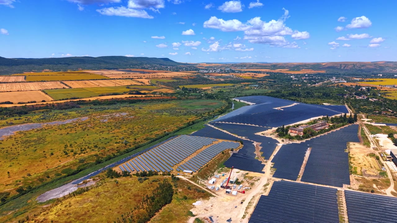 Vista aerea di un grande impianto fotovoltaico in un paesaggio rurale. Campi di pannelli solari coprono i terreni sotto un cielo blu con nuvole sparse durante il giorno