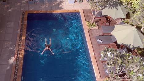 disparo de inclinación de drones sobre la piscina del hotel tropical con una joven nadando