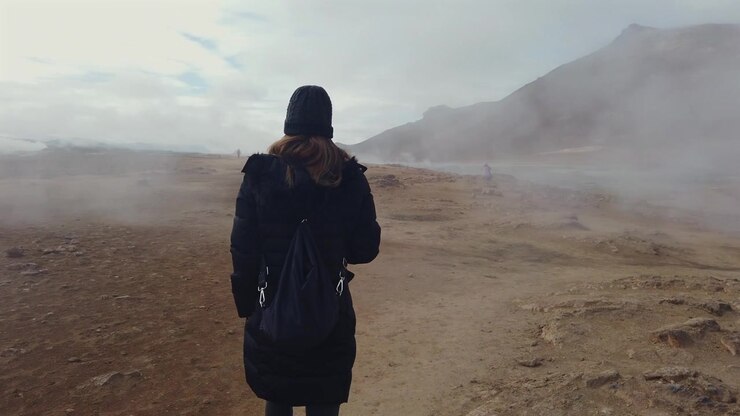Female traveler with a backpack walking along a trail in Hverir, a famous geothermal area in Iceland with steam rising from the ground