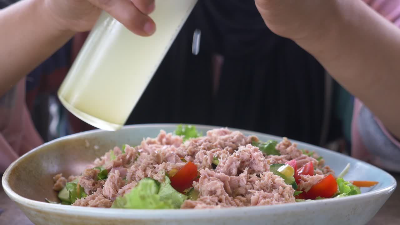 Mujer vertiendo aderezo sobre ensalada de atún