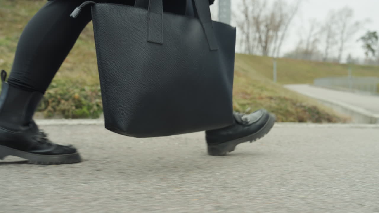 Botas caminan con confianza. Botas de cuero avanzan con paso firme. Caminando a paso firme llevando un bolso de mano en el parque. Calzado de cuero resistente se mueve ágilmente por el sendero del parque con un bolso balanceándose
