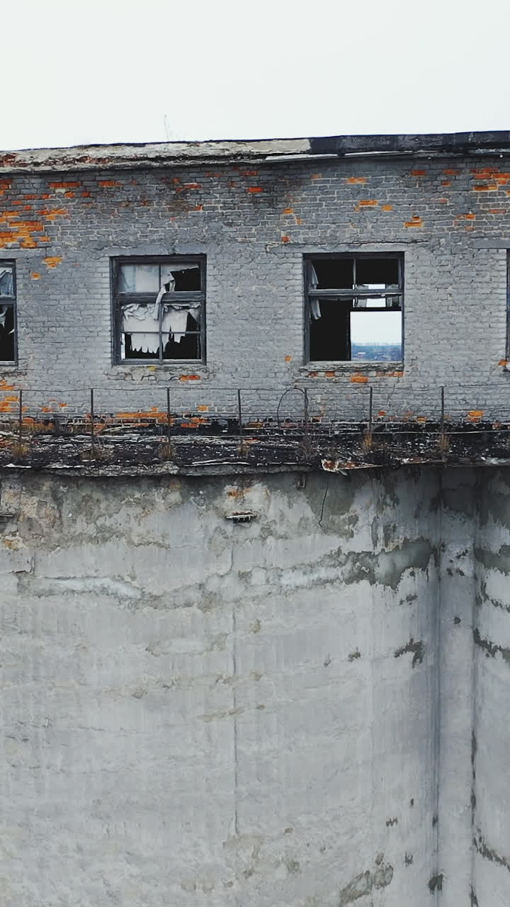 Broken windows and walls of an old chemical plant. Moss-covered concrete vault. Ruins of industrial buildings. Aerial view. Vertical video