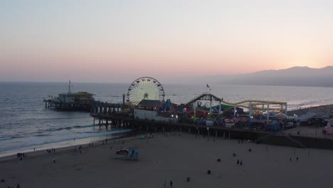 low aerial push-in shot of the busy santa monica pier on a warm summer night in southern california at twilight