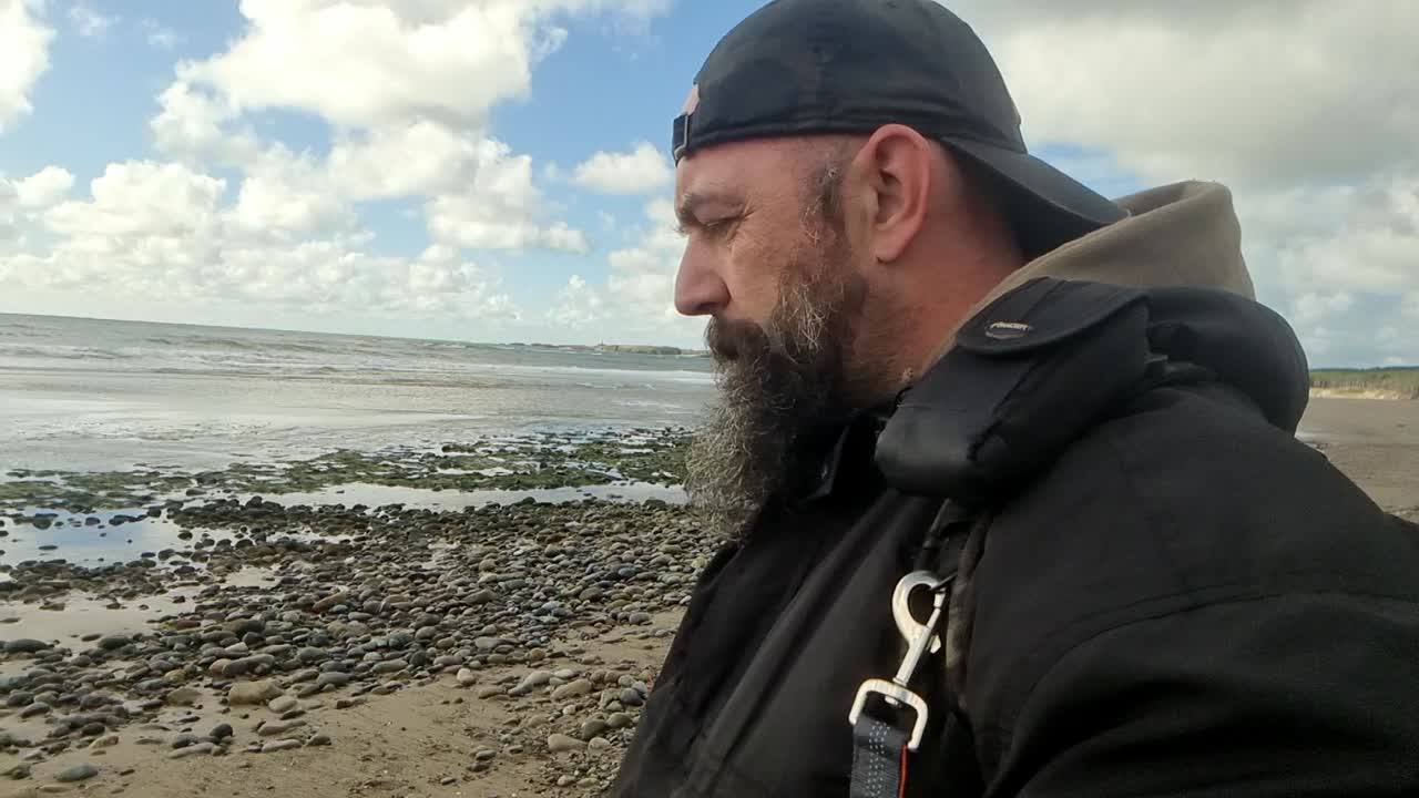 hombre barbudo problemático caminando por la playa ventosa temprano en la mañana en silencio