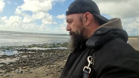 hombre barbudo problemático caminando por la playa ventosa temprano en la mañana en silencio