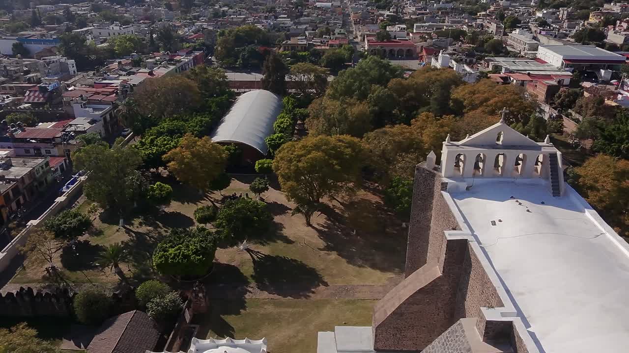 Drone glides over historic church roof revealing colorful Morelos town below, 4K