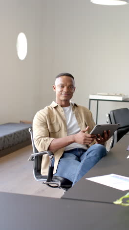 vertical video: sitting in office, man holding tablet and looking at camera confidently