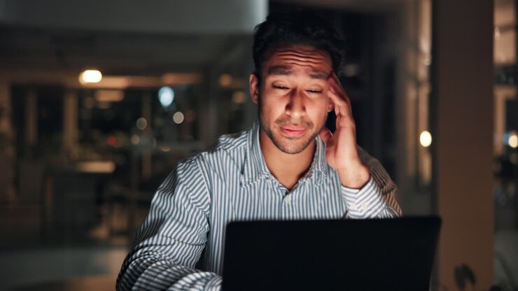 Erschöpfter Mann mit Kopfschmerzen bei langer Laptop-Arbeit