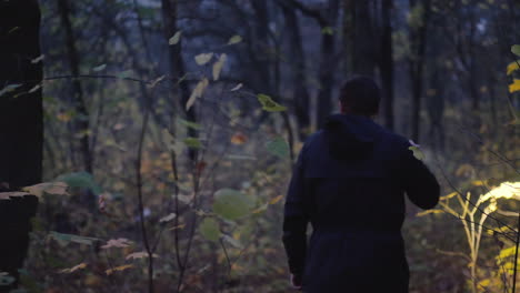 a man in a hood with a flashlight in his hand walks through a dark forest search for a man