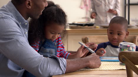 father and children drawing at table as mother prepares meal