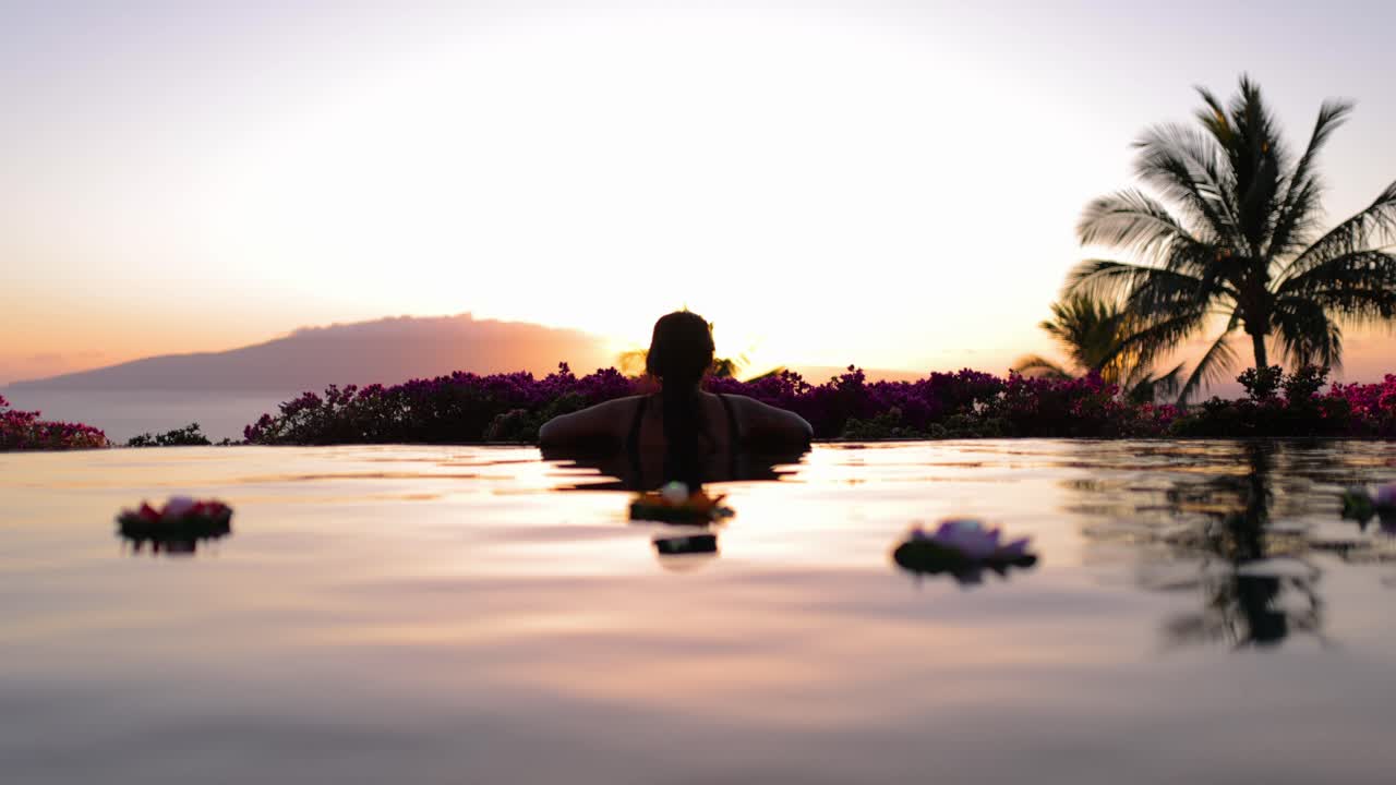 donna polinesiana tatuata guarda il tramonto dalla piscina a sfioro a maui hawaii