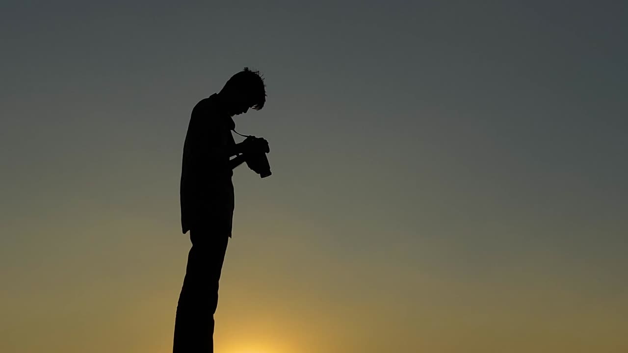 Silhouette of photographer holding DSLR camera with sunset background sky