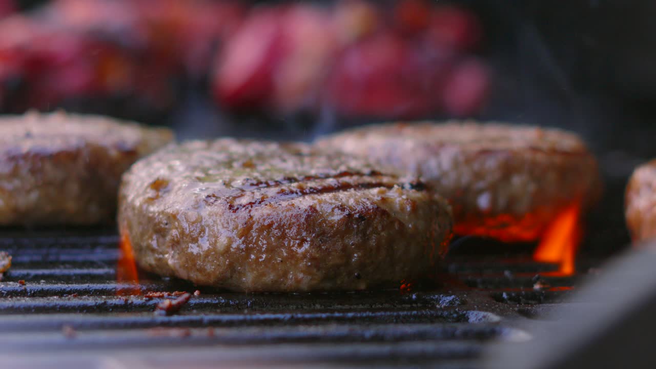 Close Up of BBQ Grill with Beef Burgers Being Cooked by Slow Motion Fire Flames Underneath Coming to Surface. Barbecue Summer Cooking Food.