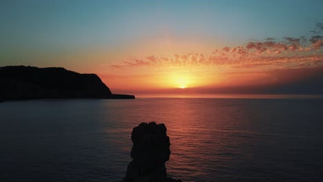 hermoso cielo naranja de la puesta de sol en el horizonte con una muñeca aérea de vuelta sobre una roca recortada frente a la playa de cala benirras en ibiza