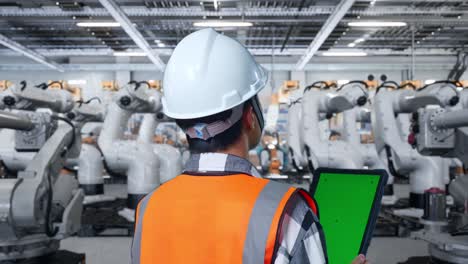 ingeniero observando brazos robóticos en una fábrica