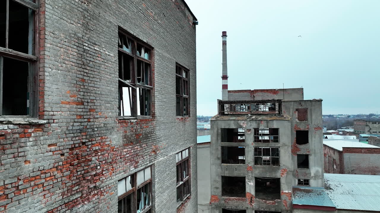 Old brick and concrete premises of an abandoned factory. Huge industrial territory with ruined constructions at the backdrop of a city.
