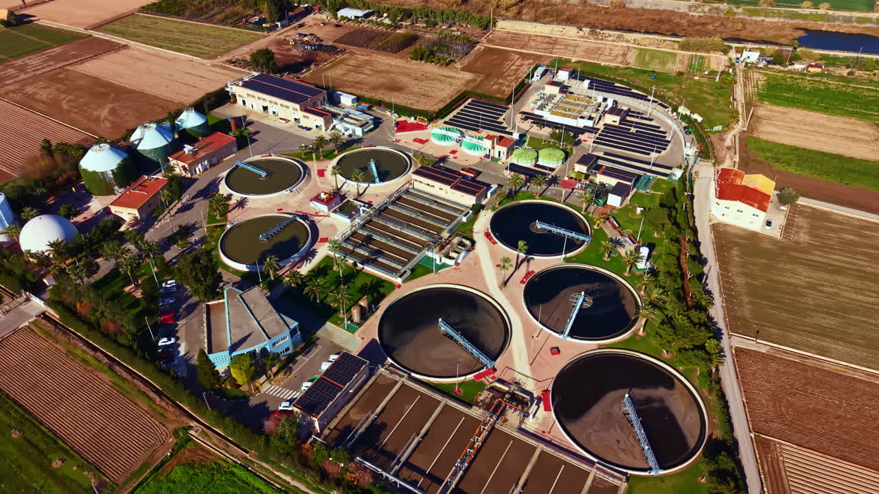 View of a water treatment facility surrounded by fields in a rural area with various tanks and buildings during the day