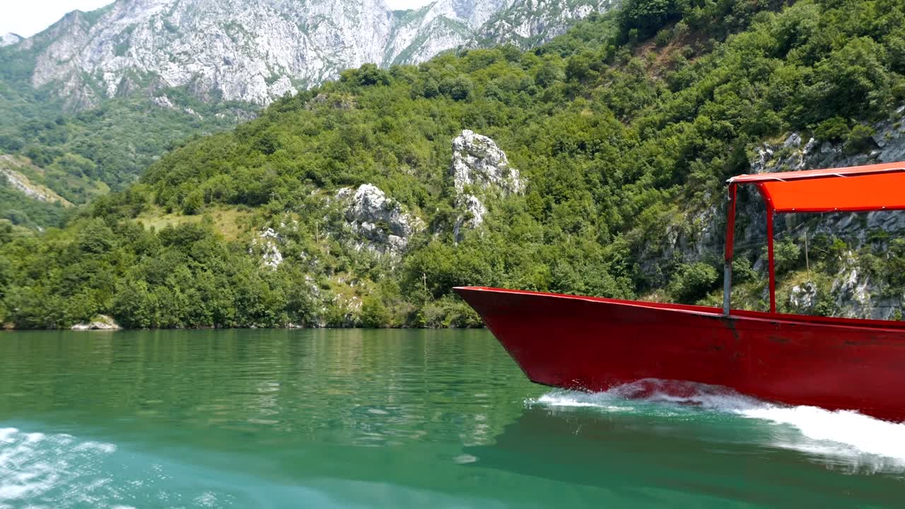 Albania, Lake Koman, bow of a red ferry on the lake's surface, with the Accursed Mountains in the background